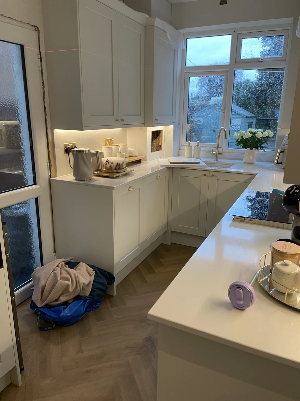 Fitted pale kitchen cabinetry and worktops beside a window